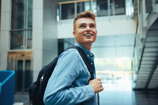 Blonde boy smiles in a grey hall with stairs in the background