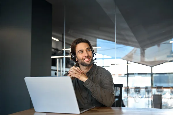 Mann mit Headset sitzt vor seinem Laptop in einem Büro